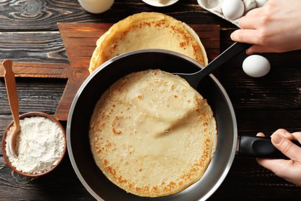 Woman cooking Russian pancakes in kitchen, closeup