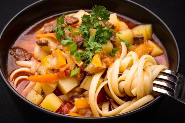 Uzbek noodle soup Lagman on black, close up, top view