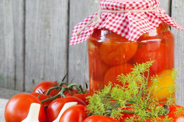 Homemade tomatoes in glass jar. Fresh and canned tomatoes on wooden board
