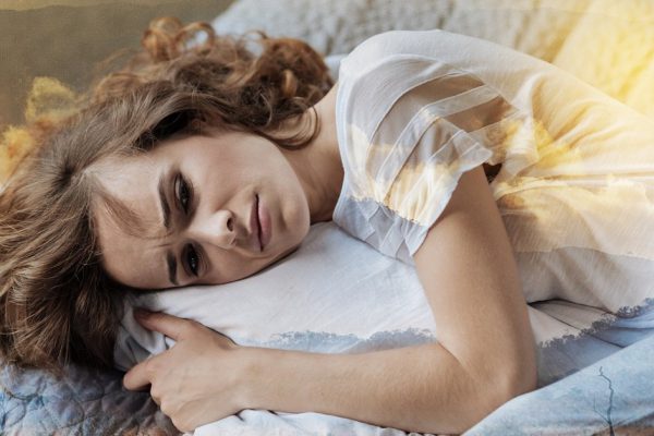 Have a problem. Young female person embracing her pillow while lying on the bed and showing her emotions