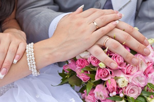 Hands of the groom and the bride on a wedding bouquet