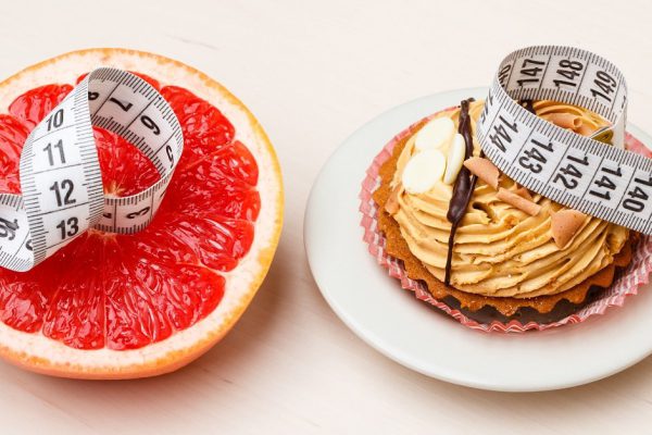 Concept of making choice: healthy low-calorie or unhealthy high-calorie food, slimming or fattening. Grapefruit and cake cupcake with measuring tape