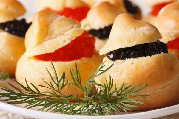 Finger food: profiteroles stuffed with red and black caviar on a plate close-up. horizontal