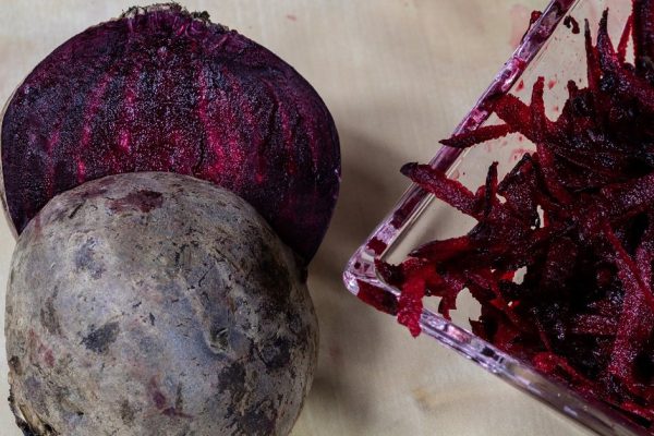 Beet grated on a kitchen grater. Kitchen countertop and preparation of salads. Dark background.