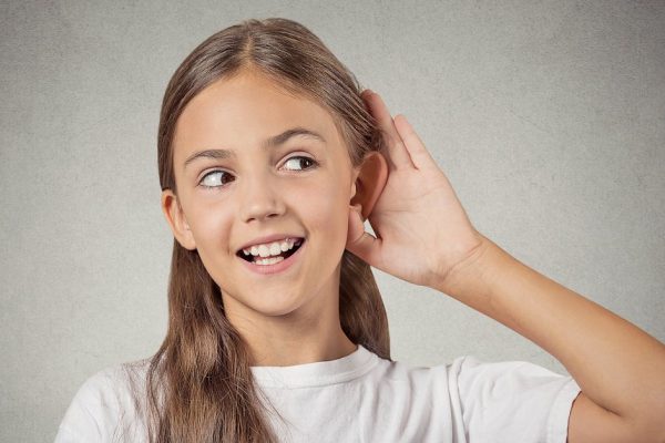 Curious girl listens. Closeup portrait teenager hearing something, parents talk, hand to ear gesture isolated grey wall background. Human face expression, emotion, body language, life perception