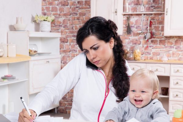 Mother with baby in the kitchen working with documents and speaks by phone