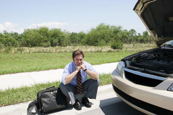 A sad looking businessman sitting on the curb waiting for the motor club.