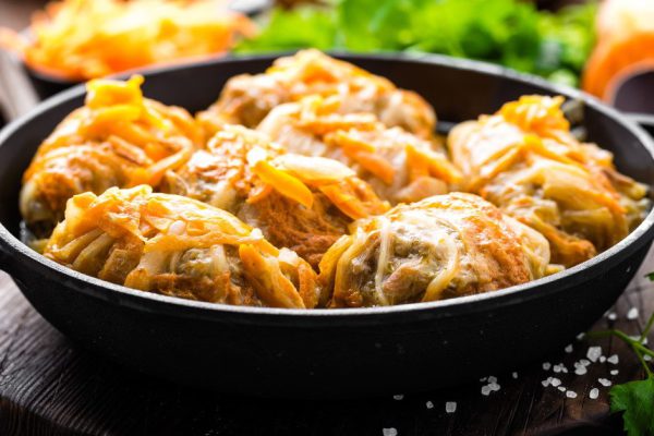 Cabbage rolls stewed with meat and vegetables in pan on dark wooden background