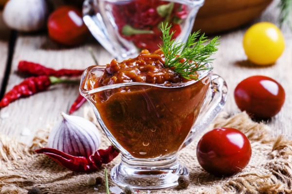 Adjika - traditional Armenian spicy sauce from tomatoes, bell peppers, garlic and spices, vintage wooden background, selective focus