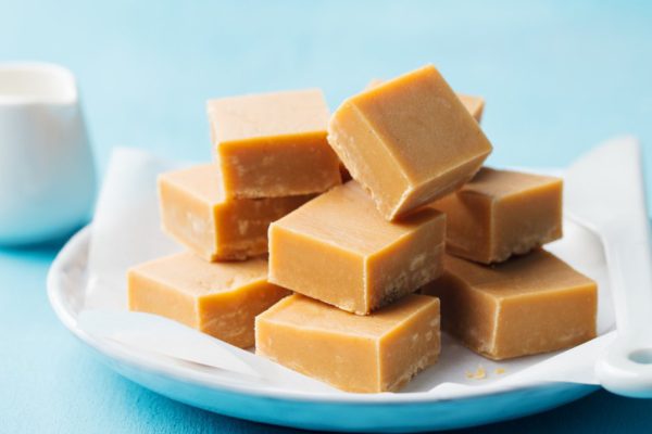Caramel fudge candies on a plate. Blue background. Close up