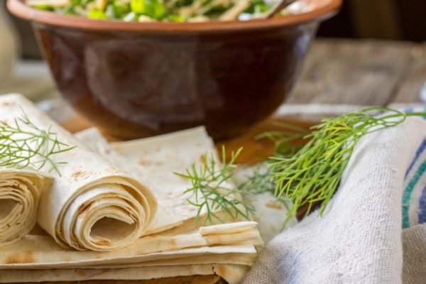 Fine homemade pita bread wrapped in a roll with fresh seasonal greens on a wooden background with home linen textiles. selective Focus