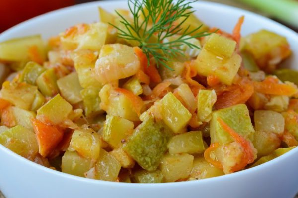 Vegetarian ragout of summer vegetables (zucchini, carrots, tomatoes, spices, garlic, chilli) in a white bowl on a wooden background. Dietary dish.