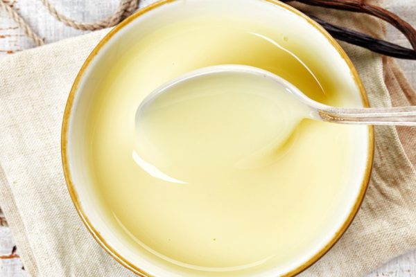 bowl of vanilla sauce on white wooden table, top view