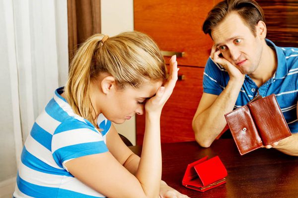 Worried couple sitting at the table with empty wallets.