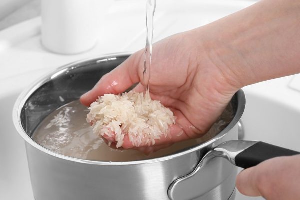 Woman rinsing rice in saucepan under running water