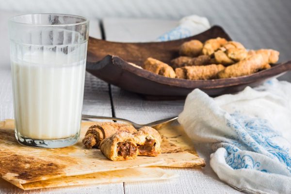 bagels biscuits from short pastry stuffed with condensed milk in a wooden plate, a glass of milk, dessert on white background