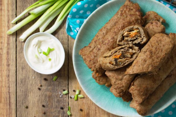 The concept of a healthy breakfast or snack. Meat liver pancakes stuffed with mushrooms and vegetables in a plate on rustic wooden table. Top view flat lay background. Copy space.