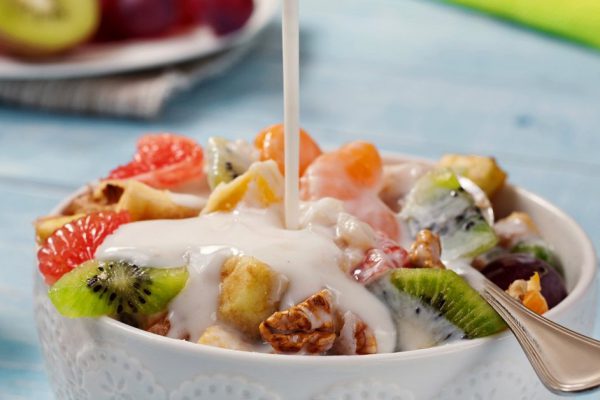 Fruit salad with yogurt and nuts closeup. Yogurt pouring in a fruit salad. Copy space