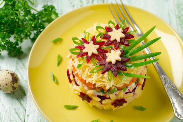 Vegetable salad with spring decoration. Layered salad in a glass dish on a blue wooden background