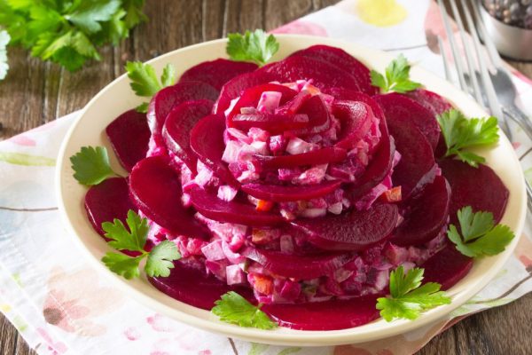 Festive salad an appetizer in the form of rose (from beetroot, eggs, pickled cucumber, potatoes, herring) on the old wooden background.