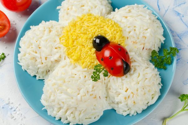 Festive salad shaped chamomile with a ladybug tomato and olives. Salad topped with grated egg
