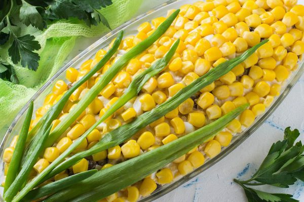 Delicious festive salad with eggs, cheese, prunes and canned corn. The original form of an ear of corn. Creative idea for holiday meals