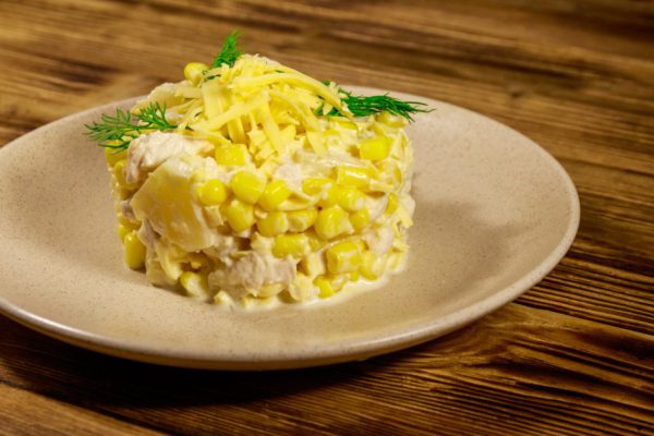 Festive salad with chicken breast, sweet corn, canned pineapple, cheese and mayonnaise on wooden table