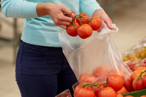 sale, shopping, food, consumerism and people concept - woman with bag buying tomatoes at grocery store