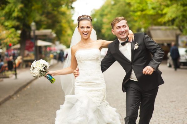 Newlyweds are walking on the street with smile. They are hugging each other and looking exciting.