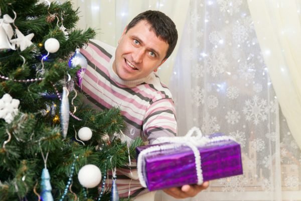 The man holds a gift at the Christmas tree in home interior