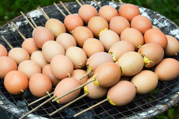Eggs grilled with bamboo stick on grill hot stove in street food market thailand / egg seasoning