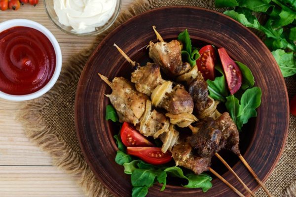 Pieces of meat with onions on skewers (kebab). Serve with sauce, tomatoes and arugula. top view