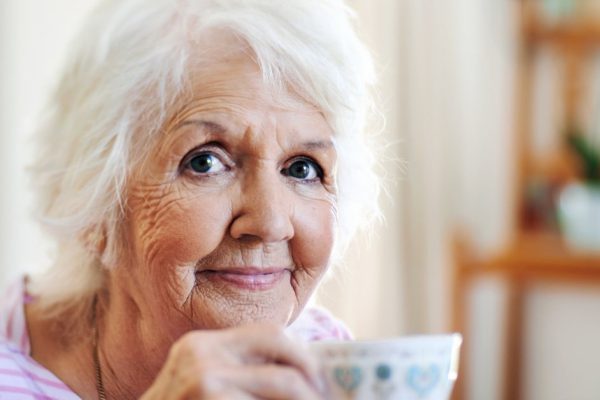 An old lady holding a cup of tea and smiling at the camera