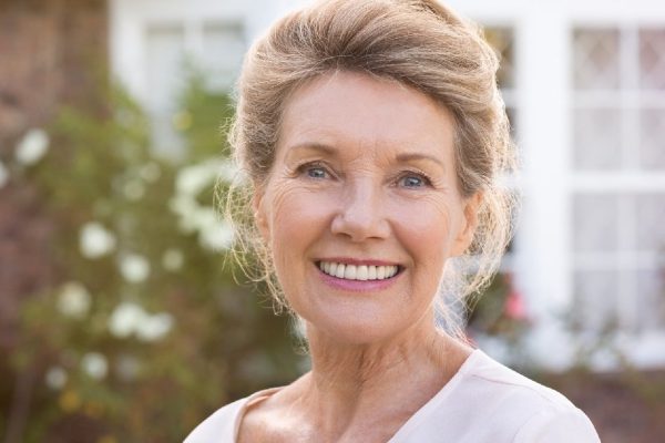 Happy senior woman standing outside her house. Content woman smiling and looking at camera. Portrait of cheerful old grandmother relaxing outside the house.