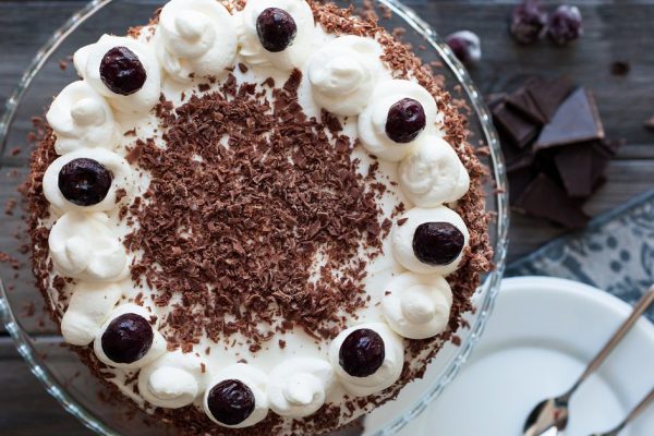 Black forest cake decorated with whipped cream, cherries and with chocolate chips on a dark wooden background. Top view.
