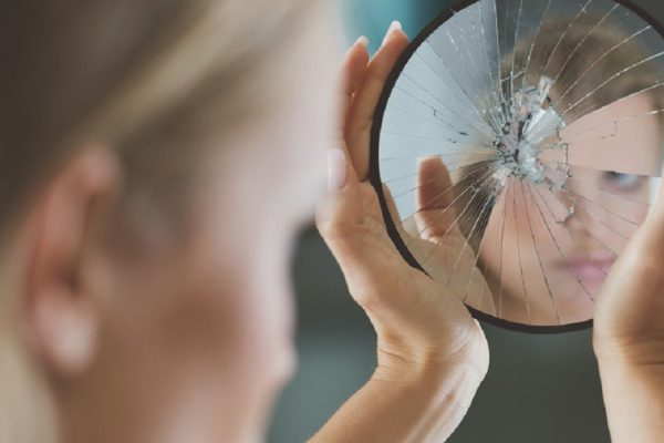 Woman with mental disorder holding small broken mirror
