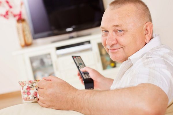 Middle aged man sitting on sofa holding remote control and cup watching television indoor