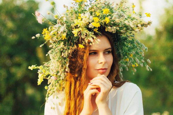 beautiful girl in wreath of flowers  in meadow on sunny day. Portrait of Young beautiful woman wearing a wreath of wild flowers. Young pagan Slavic girl conduct ceremony on Midsummer.