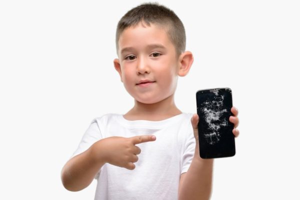Dark haired little child holding broken smartphone very happy pointing with hand and finger