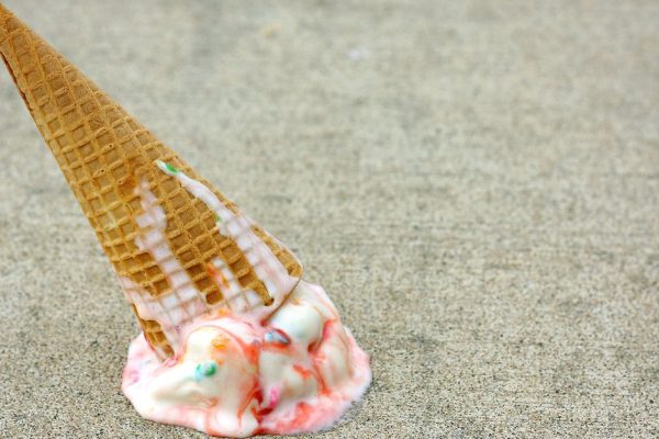 A rainbow colored ice cream cone has dropped upside down on the sidewalk on a summer day
