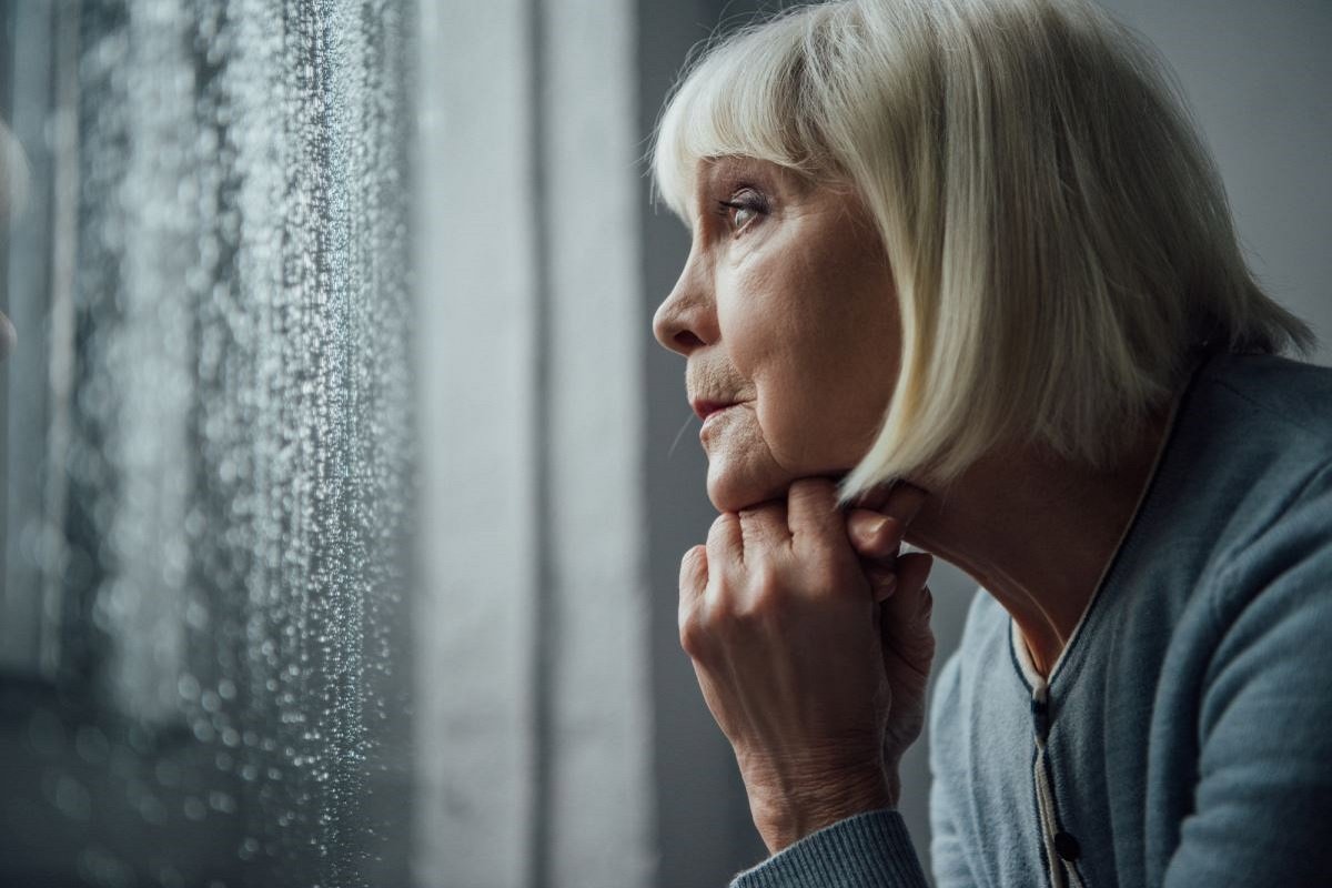 женщина смотрит в окно и грустит