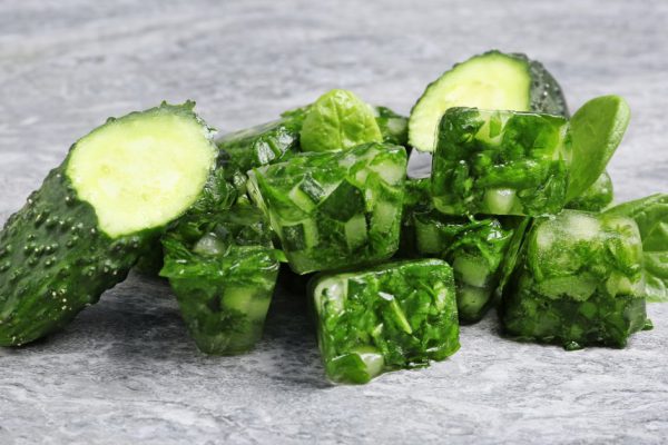Vegetable ice cubes and fresh cucumbers on grey table