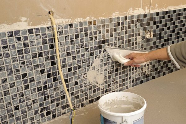 A wall partly covered with mosaic tiles, and an arm grouting.