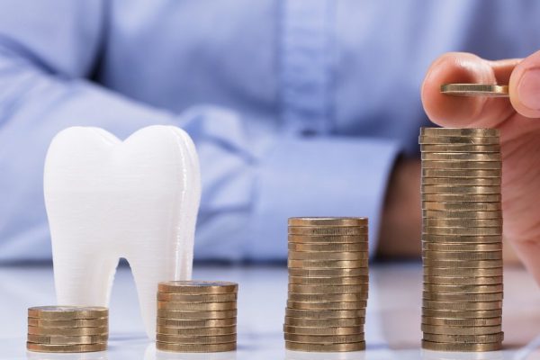 Man Placing Coin On Top Of The Stack Coins In Front Of White Tooth
