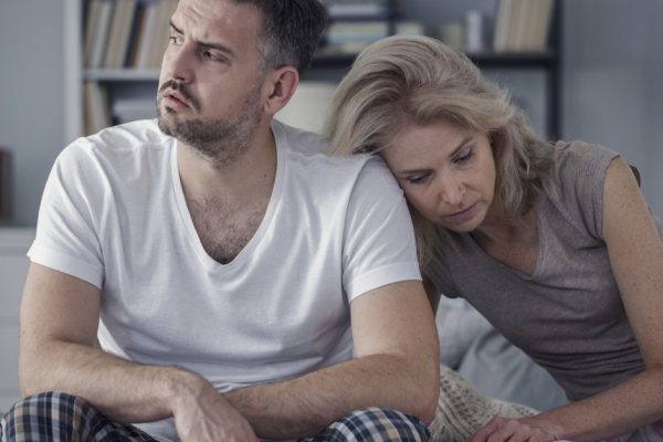 Unhappy husband and sad wife sitting together in the bedroom. Difficult marriage concept