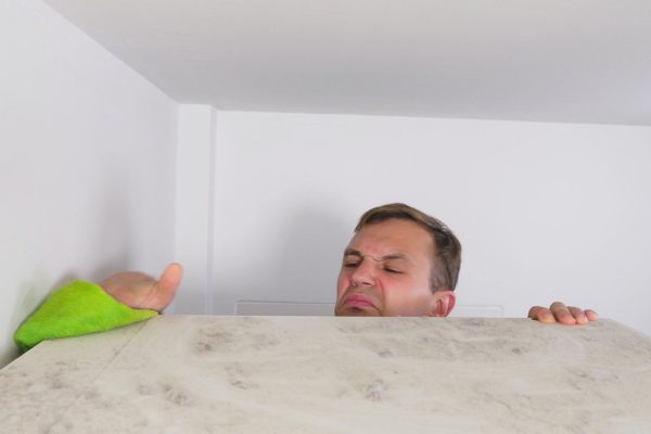 home cleaning concept. a man wipes dust from a high cabinet in his house.