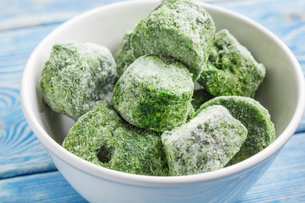 Frozen spinach blocks in white bowl. Selective focus.