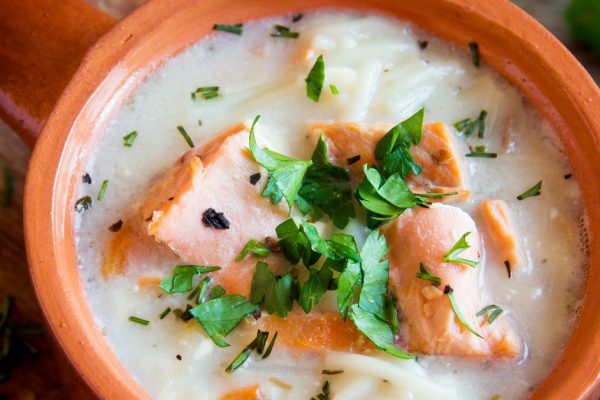 Salmon soup with noodles and vegetables in ceramic bowl close up