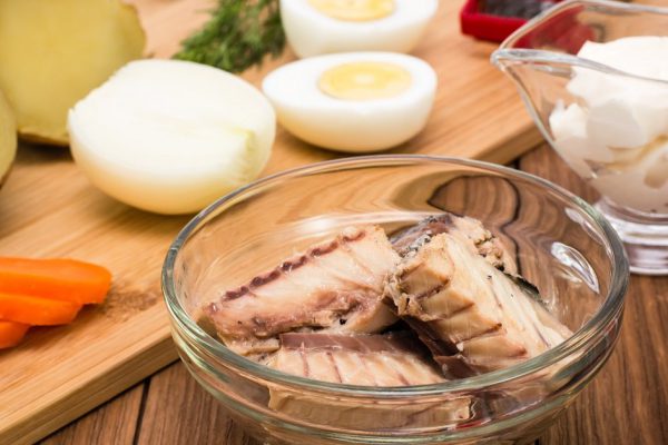 Canned sardines in a bowl and ingredients for the preparation of Mimosa salad
