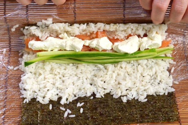cooking rolls of rice, fish, cucumber and nori on a bamboo mat at home with their own hands. Japanese cuisine.